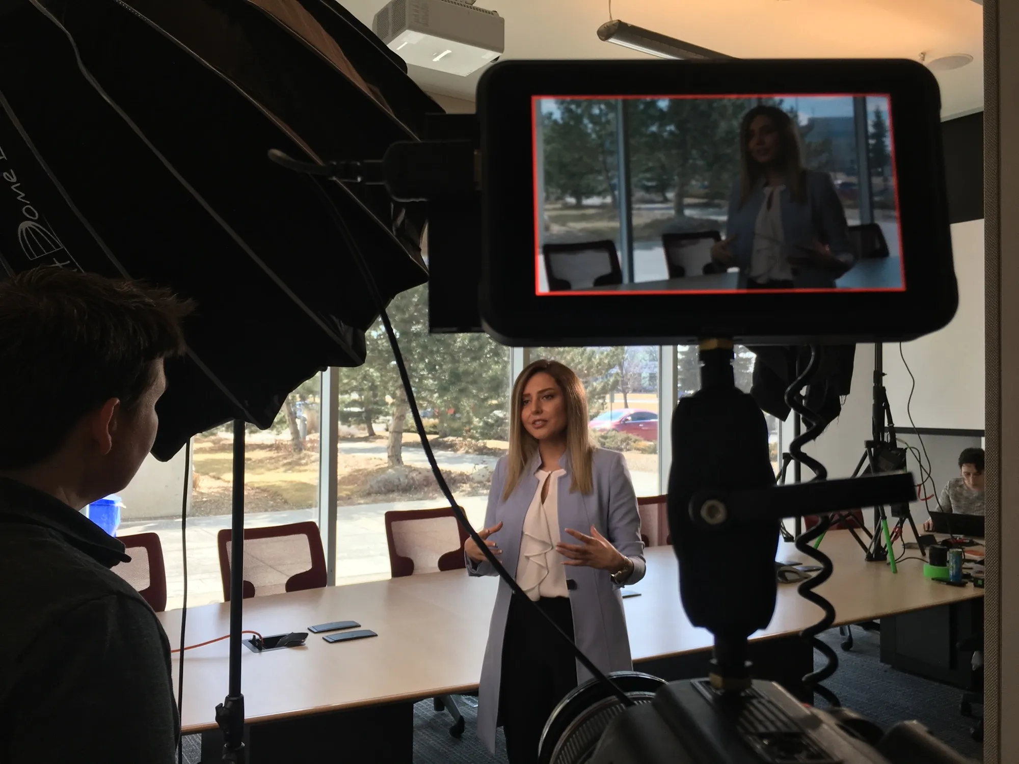 On set in a boardroom: a camera monitor in the foreground frames a presenter mid-talk under studio lighting.